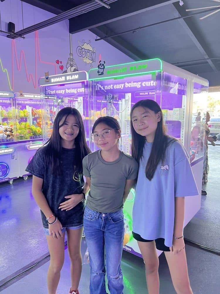 Three friends standing together in front of the claw machines.